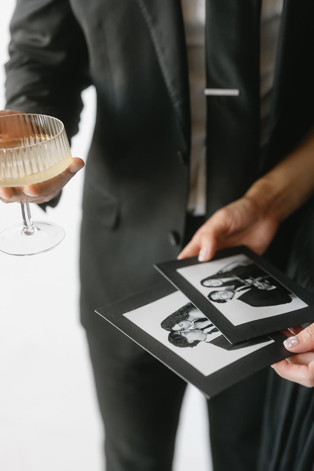 Hands holding elegant photo booth prints alongside a cocktail